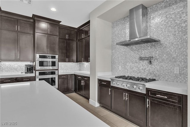 kitchen with light tile patterned floors, wall chimney exhaust hood, stainless steel appliances, light countertops, and backsplash