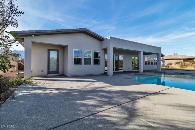 rear view of property featuring a fenced in pool, a patio, and stucco siding