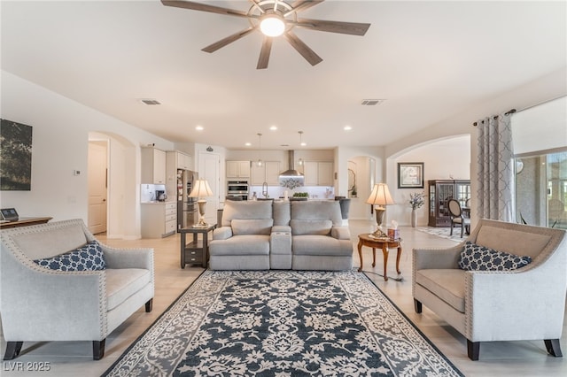 living area with visible vents, arched walkways, a ceiling fan, light wood-type flooring, and recessed lighting