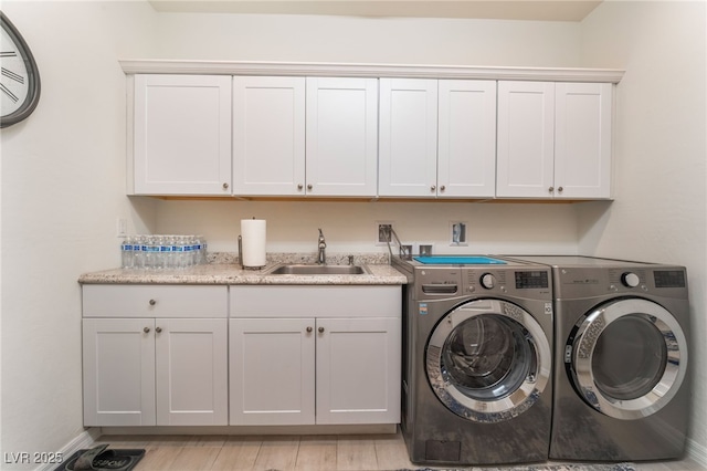 laundry room with washing machine and clothes dryer, cabinet space, a sink, light wood-type flooring, and baseboards