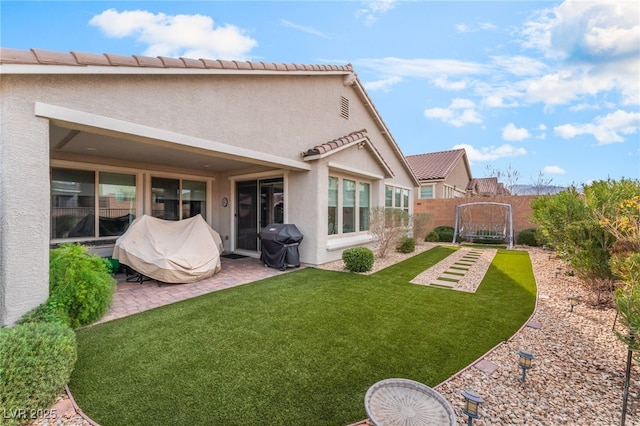 rear view of house featuring fence, a lawn, a patio, and stucco siding