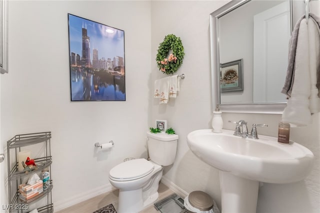 half bath with toilet, a sink, baseboards, and a city view