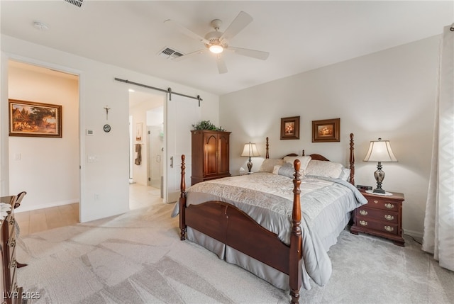 bedroom featuring ensuite bathroom, a barn door, light carpet, visible vents, and a ceiling fan