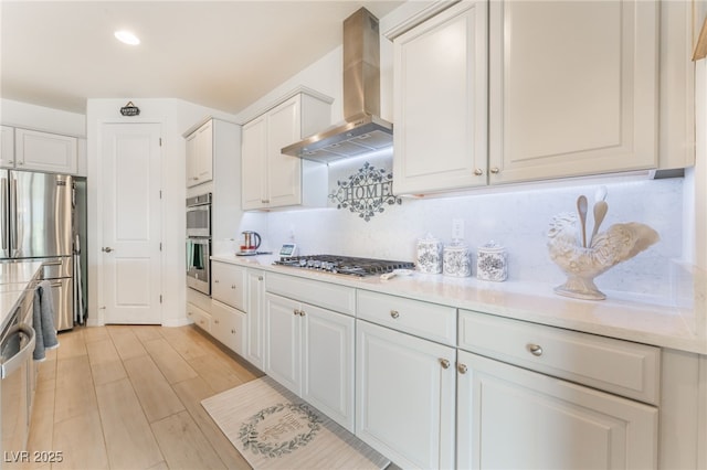 kitchen featuring stainless steel appliances, white cabinetry, backsplash, and wall chimney exhaust hood