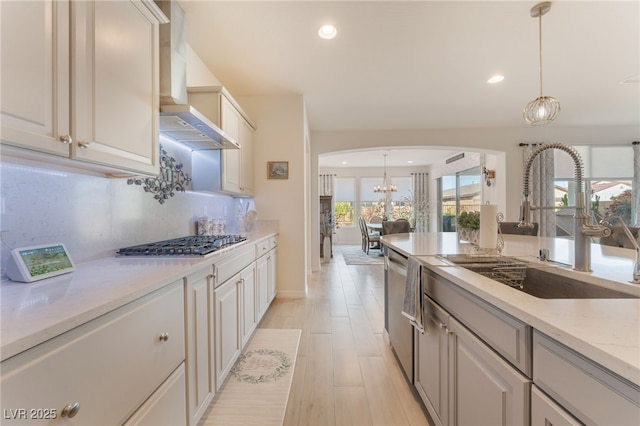 kitchen featuring tasteful backsplash, arched walkways, wall chimney exhaust hood, appliances with stainless steel finishes, and a sink