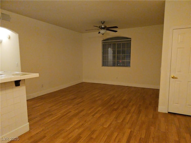 unfurnished room featuring visible vents, baseboards, a ceiling fan, arched walkways, and wood finished floors