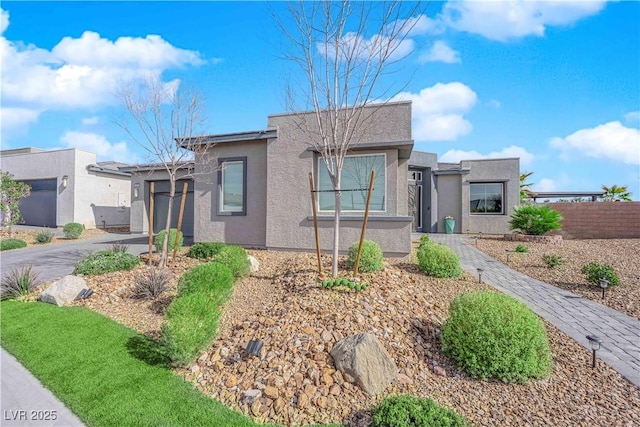 view of front facade featuring driveway, an attached garage, fence, and stucco siding