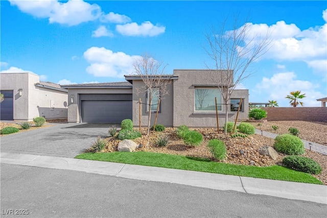 view of front of house with decorative driveway, stucco siding, fence, a garage, and a tiled roof