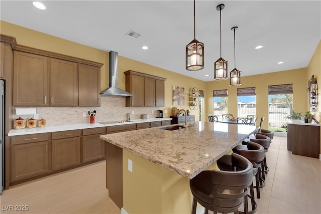 kitchen featuring decorative backsplash, an island with sink, wall chimney exhaust hood, black electric cooktop, and a sink