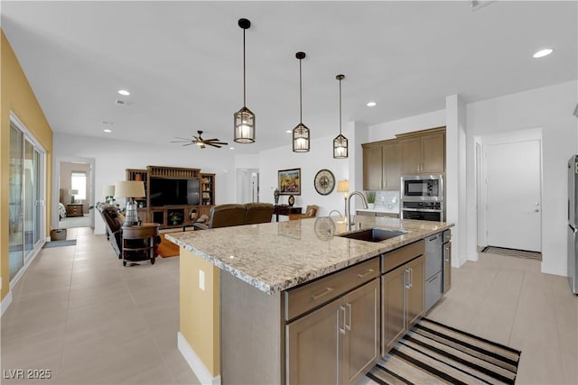 kitchen featuring light stone counters, stainless steel appliances, a sink, an island with sink, and decorative light fixtures