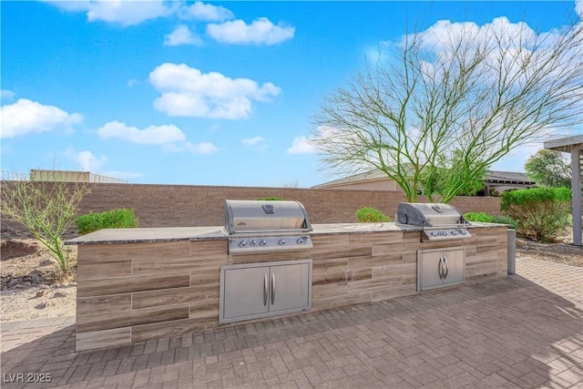 view of patio with a grill, fence, and an outdoor kitchen