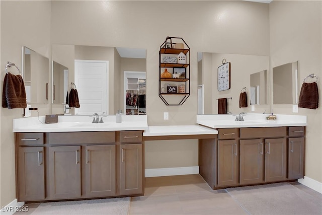 full bath with two vanities, a sink, a spacious closet, and baseboards