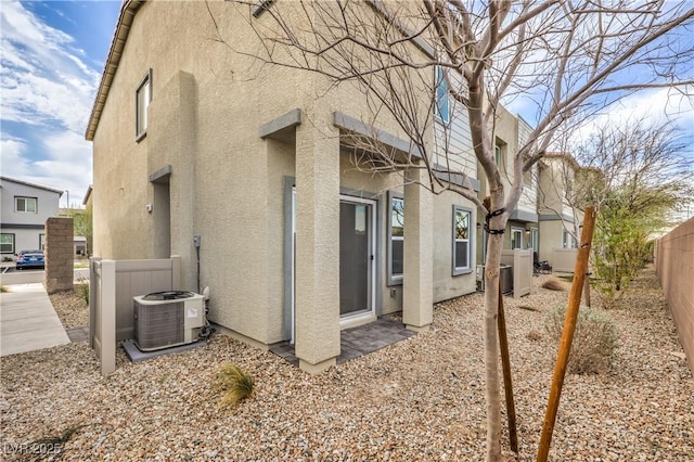 view of side of property featuring central AC, fence, and stucco siding