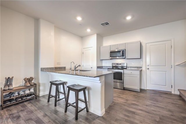 kitchen with stainless steel appliances, a breakfast bar, a sink, visible vents, and dark stone countertops