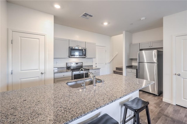 kitchen featuring light stone counters, stainless steel appliances, gray cabinets, visible vents, and a sink