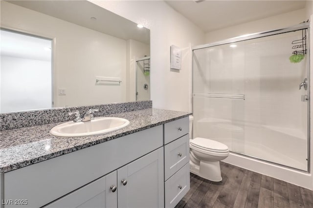 bathroom with toilet, a stall shower, wood finished floors, and vanity