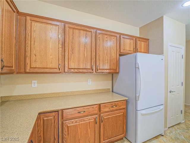 kitchen featuring brown cabinets, light countertops, and freestanding refrigerator