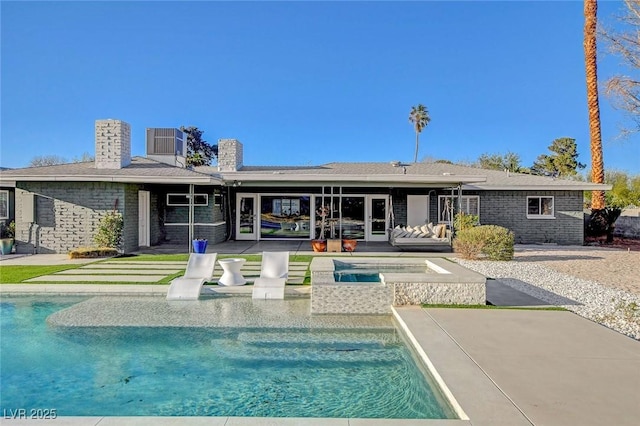 back of property with an outdoor pool, a patio, a chimney, an in-ground hot tub, and brick siding