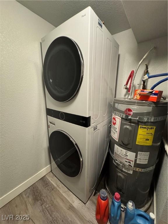 laundry area featuring laundry area, baseboards, stacked washer / drying machine, wood finished floors, and water heater