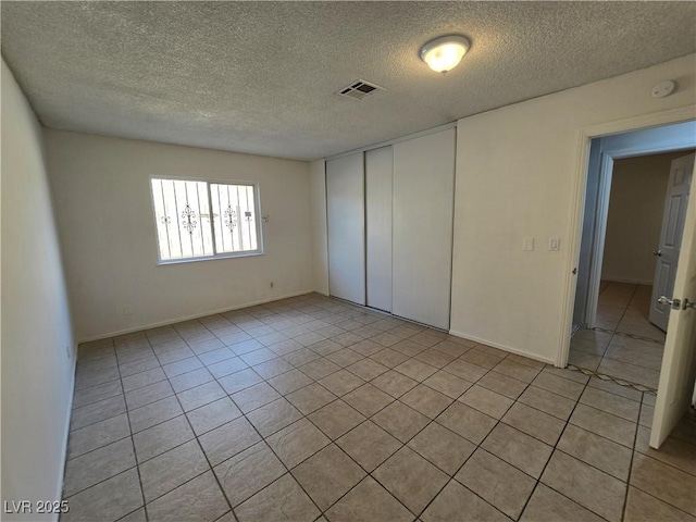 unfurnished bedroom featuring light tile patterned floors, a closet, a textured ceiling, and visible vents