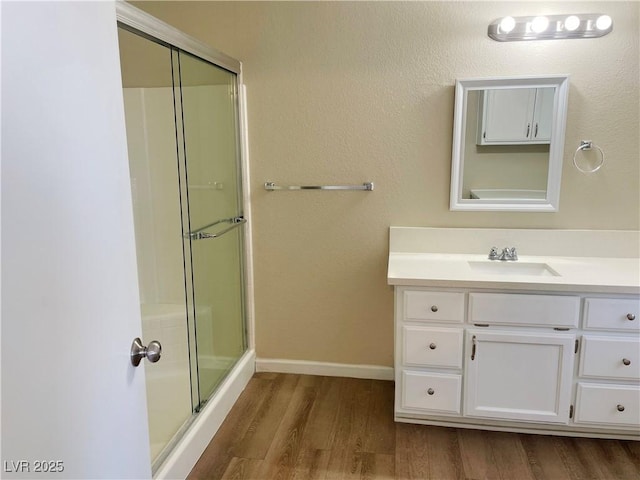 bathroom with wood finished floors, an enclosed shower, vanity, and baseboards