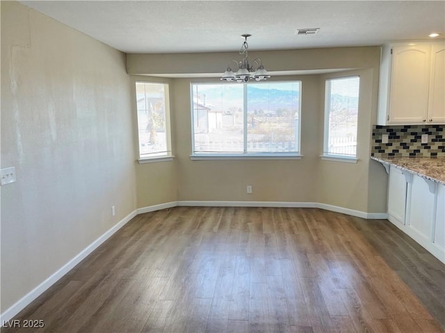 unfurnished dining area featuring a chandelier, wood finished floors, visible vents, and baseboards