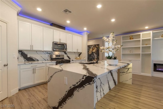 kitchen featuring visible vents, white cabinets, an island with sink, stainless steel appliances, and light wood-style floors