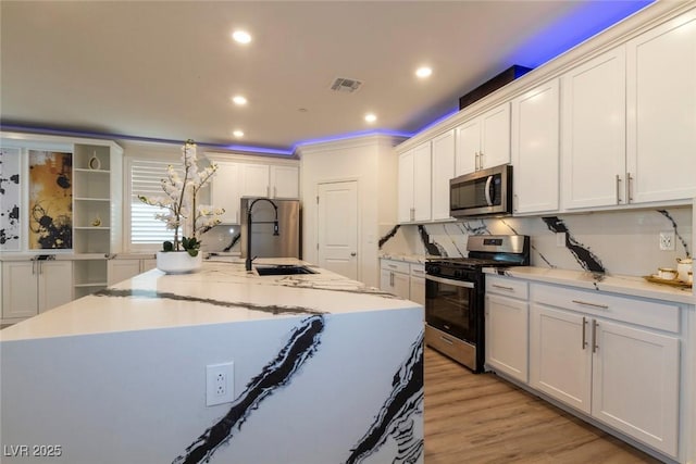 kitchen featuring stainless steel appliances, visible vents, light wood-style flooring, a kitchen island with sink, and a sink