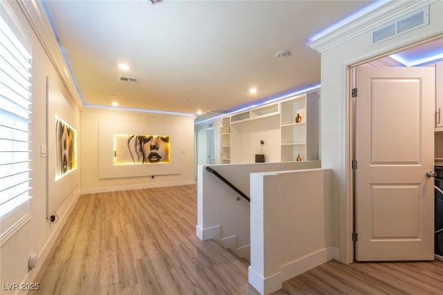 hallway featuring light wood finished floors, recessed lighting, visible vents, ornamental molding, and an upstairs landing