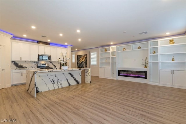 kitchen featuring stainless steel appliances, light wood finished floors, an island with sink, and white cabinets