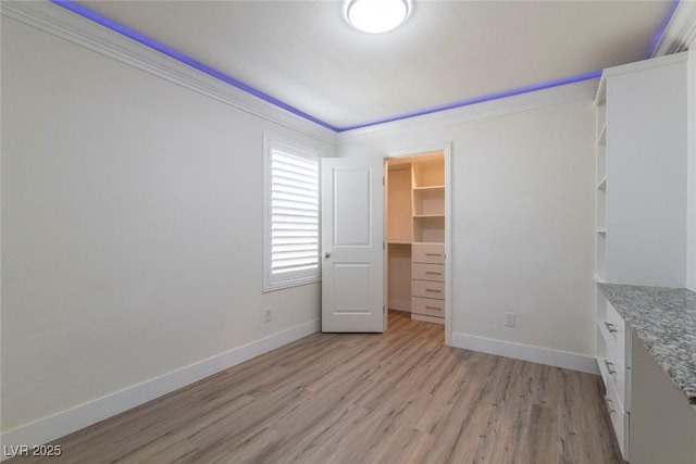 unfurnished bedroom with baseboards, light wood-style flooring, ornamental molding, a spacious closet, and a closet