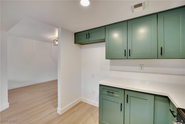 kitchen with light wood-type flooring, visible vents, green cabinets, and light countertops