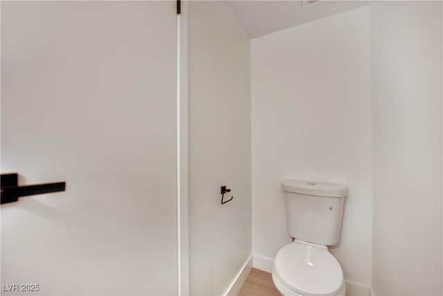 bathroom with toilet, baseboards, and wood finished floors