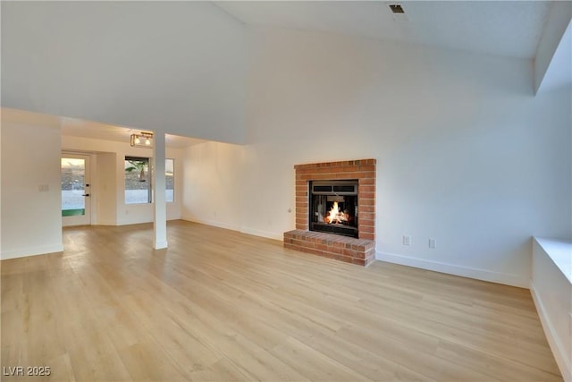 unfurnished living room with baseboards, high vaulted ceiling, a brick fireplace, and light wood-style floors