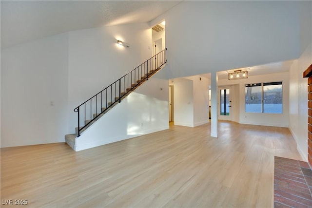 unfurnished living room with visible vents, stairs, high vaulted ceiling, and wood finished floors