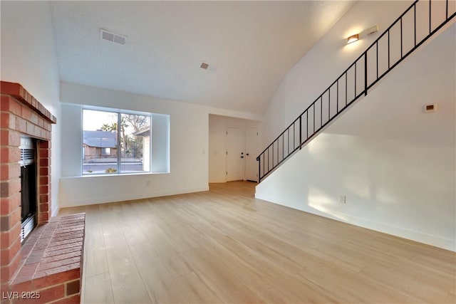 unfurnished living room with visible vents, lofted ceiling, stairway, wood finished floors, and a brick fireplace