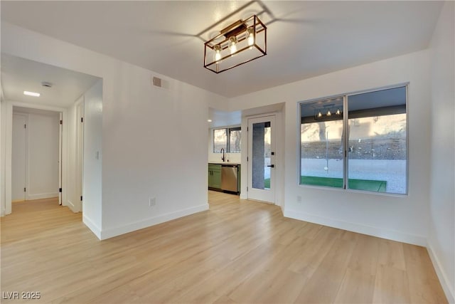 spare room with light wood finished floors, a sink, visible vents, and baseboards