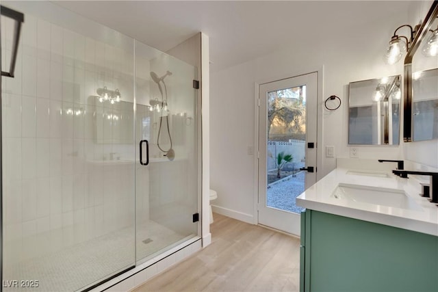 full bathroom featuring double vanity, toilet, a sink, a shower stall, and wood finished floors