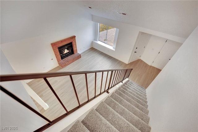 stairs featuring a brick fireplace, visible vents, and wood finished floors