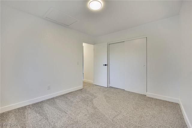 unfurnished bedroom with light carpet, a closet, attic access, and baseboards