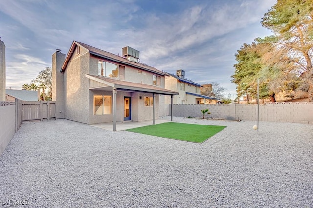 rear view of house with stucco siding, a fenced backyard, cooling unit, and a patio