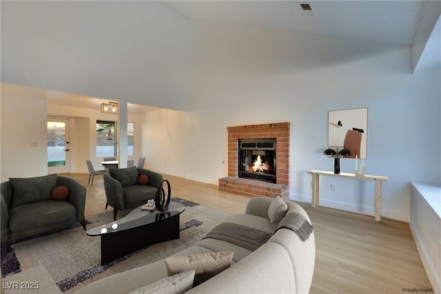 living room featuring high vaulted ceiling, a brick fireplace, light wood-style flooring, and baseboards