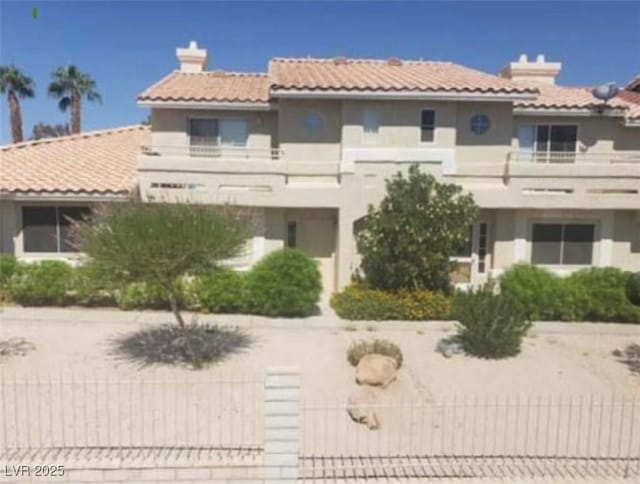 view of front of home with driveway, a chimney, a tile roof, and a balcony