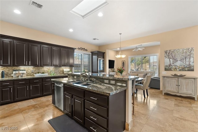 kitchen featuring tasteful backsplash, stainless steel dishwasher, open floor plan, a sink, and plenty of natural light