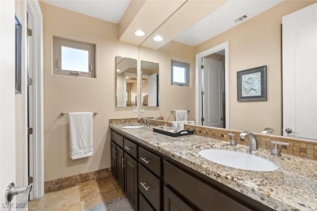 bathroom with double vanity, baseboards, visible vents, and a sink