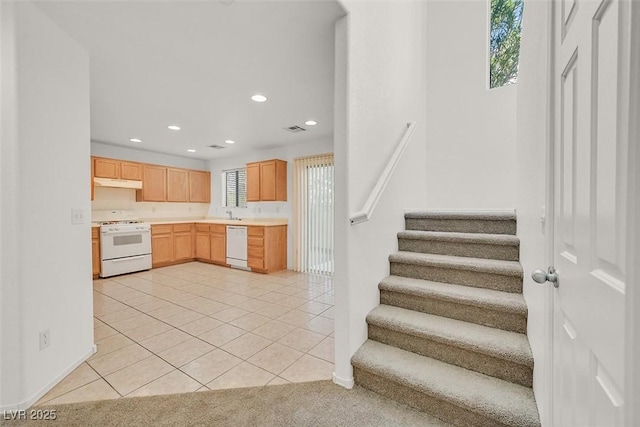 kitchen featuring visible vents, light brown cabinets, under cabinet range hood, light countertops, and white appliances