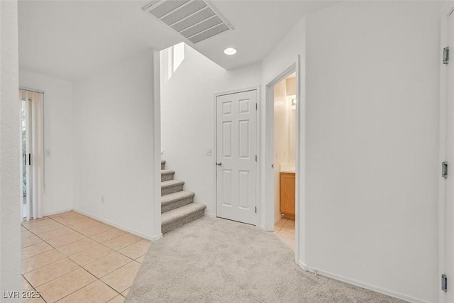 interior space featuring visible vents, baseboards, stairway, light tile patterned floors, and light carpet