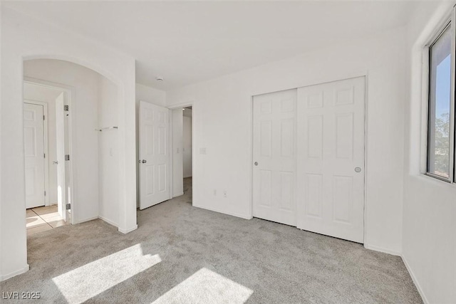 unfurnished bedroom featuring a closet, baseboards, carpet, and arched walkways