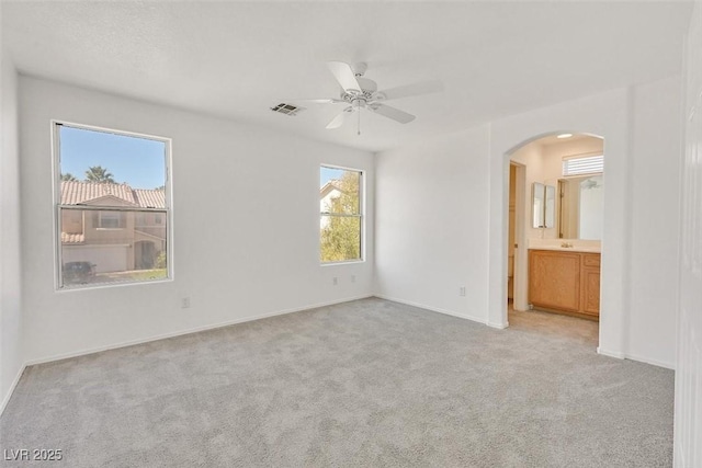 unfurnished bedroom featuring baseboards, visible vents, ensuite bath, arched walkways, and light carpet