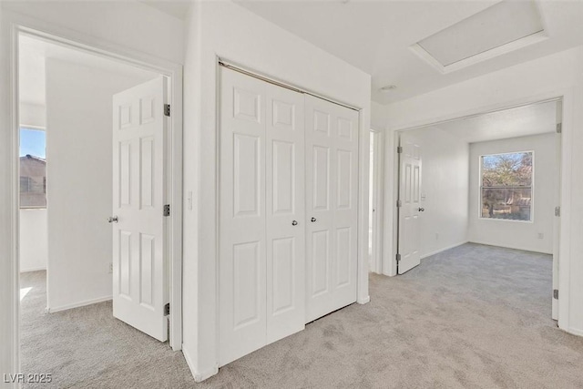 hall featuring baseboards, light colored carpet, and attic access